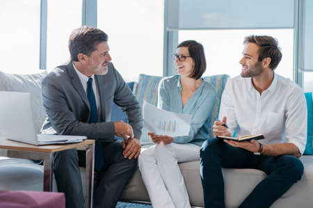 Group of successful businesspeople discussing paperwork and using a laptop together while sitting on...