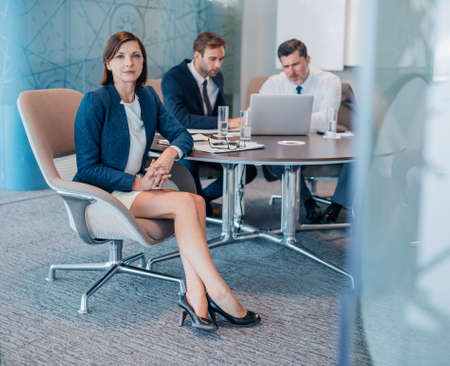 Portrait of a confident young businesswoman sitting at a table with colleagues working in the...