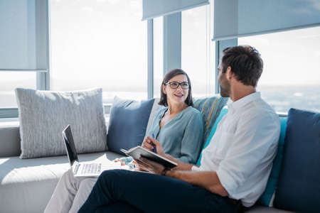 Two confident young businesspeople using a laptop and reading notes together while sitting on a sofa...