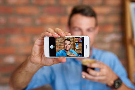 Young man taking a selfie with his phone while drinking a coffee
