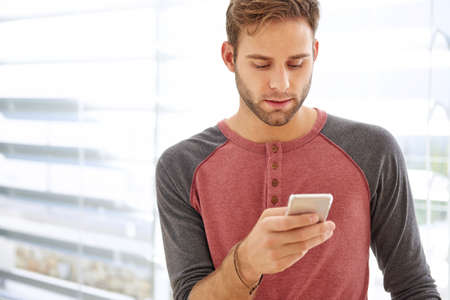 Handsome man with fashionable stubble in casual clothes, reading a text message on his modern phone...