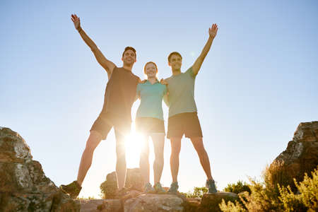 Low angle shot of three athletic friends standing on a rocky mountain and posing triumphantlyの写真素材