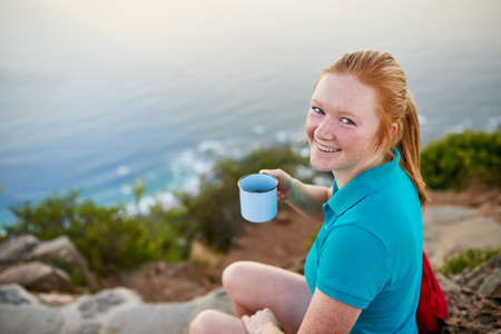 Smiling young woman looking at the camera with a cup of coffee on an early morning hike