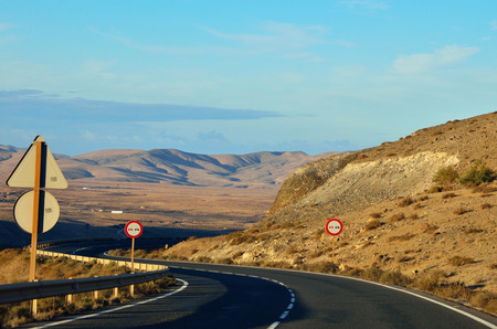 road with white lines under clouds and blue sky near the mountains and srone desert on the island (Fuerteventura)の写真素材