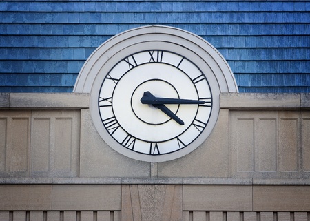 Big outside clock with Roman Numerals on stone building with blue roofの写真素材
