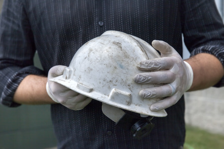 One man holding safety hardhat wearing rubber gloves outside の写真素材