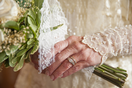 hand of older bride in vintage dress showing rings and holding bouquet of flowersの写真素材