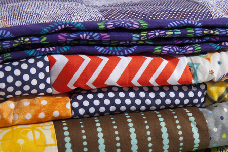 A close up of stacked quilts showing different patterns and cloth texture.