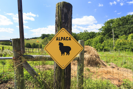 Alpaca crossing sign on a fence post in front of a large farmの写真素材