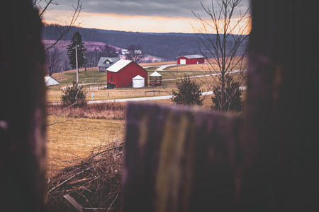 Pennsylvania farm filtered style. Red barn and silo and farm houses are visible. Framed by wooden fence. Winter.の写真素材