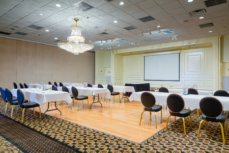 Empty hotel conference meeting room with chairs and tables set up before a white projection screenの写真素材