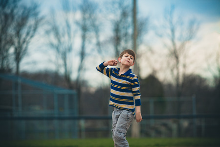 Caucasian autistic boy in striped shirt pretends to throw a ball outsideの写真素材