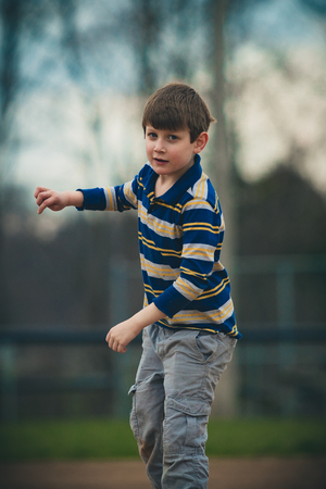 Caucasian autistic boy in striped shirt pretends to throw a ball outsideの写真素材