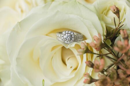 Close up macro of bridal diamond wedding band and engagement ring placed in brides floral bouquetの写真素材