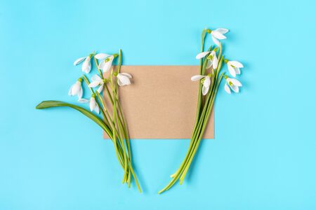 bouquet of flowers of snowdrops and craft paper for notes on blue background Flat lay Top view Holiday card Hello Spring concept Mock up.の写真素材