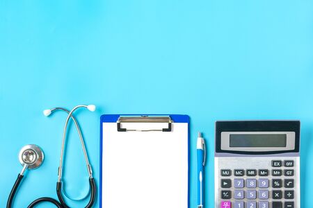 Phonendoscope, calculator, tablet with white paper, pen on blue background Diagnosis, health, life, medical Insurance concept Top view Flat lay Mock up.の写真素材