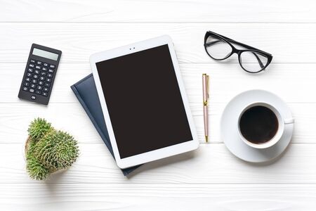 Home office workspace. Tablet, glasses, notepad, cup of coffee, pen, succulent on white wooden background. Top view Business, freelance work concept Mock up Flat lay.の写真素材