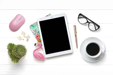 Home office workspace. Tablet, calculator, notepad, golden pen and clips, glasses, flamingo figurine, cup of coffee, succulent, pc mouse on white wooden background. Top view Mock up Flat lay.の写真素材