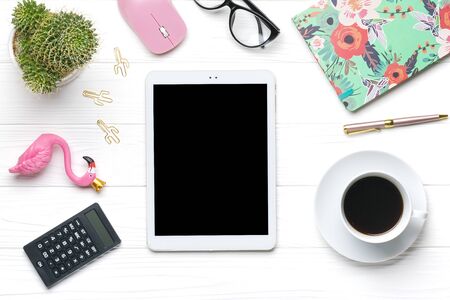 Home office workspace. Tablet, calculator, notepad, golden pen and clips, glasses, flamingo figurine, cup of coffee, succulent, pc mouse on white wooden background. Top view Mock up Flat lay.の写真素材
