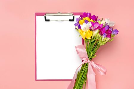 Bouquet of sprig freesia flowers, tablet with white paper isolated on pink background Floral holiday card Top view Flat lay.の写真素材