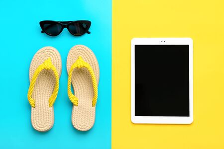 Swimming accessories - trendy black glasses, summer flip flop, tablet on blue, yellow background Flat lay Top view Travel, vacation, online booking concept Mock up.の写真素材