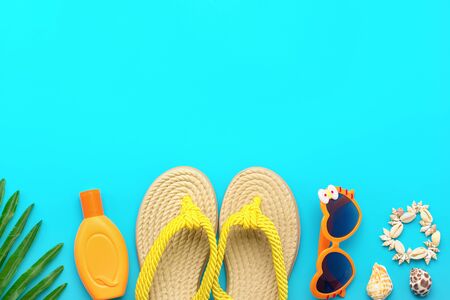 Swimming accessories - trendy beach bag with stripes, sunblock, heart - shaped glasses, flip flop, palm, shells, tablet on blue background Flat lay Top view Travel, vacation, online booking conceptの写真素材