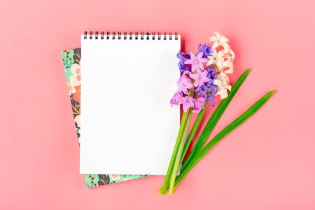 Workplace with bouquet of hyacinths flowers, white notepad on pink background Flat lay Top view copy space Mock up Sesonal, education concept Floral holiday card Place for text.の写真素材