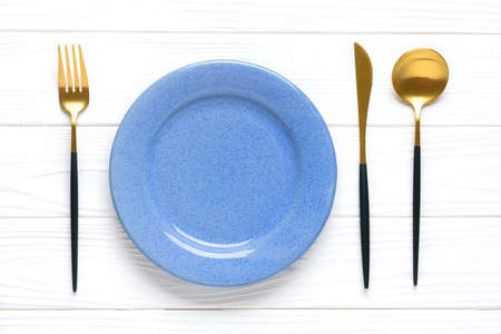 empty white round blue plate, fork, knife, spoon on wooden table Top view Flat lay Dishes for...