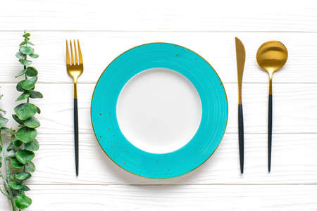 empty round blue plate, fork, knife, spoon, sprig of eucalyptus on wooden table Top view Flat lay...