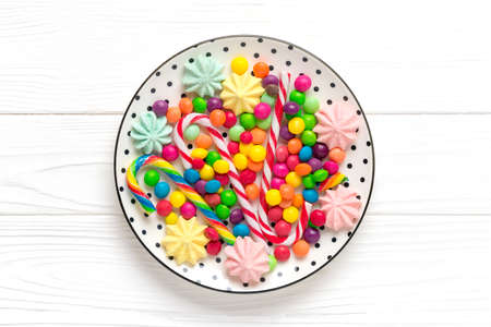mix colorful sweets - white round plate with black peas, lollipop, meringue, chocolate, sprinkle on wooden background Flat lay Top view Holiday card Happy birthday party concept.の写真素材