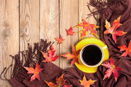 cup with black coffee, brown textile scarf, wooden table with red, yellow autumn fallen orange...