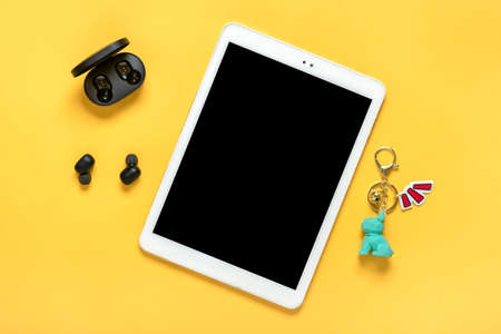 Tablet with black screen and wireless headphones, charger capsule on yellow background Mock up Flat...