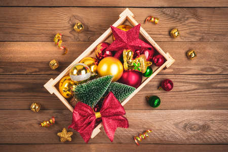 box with Christmas toys - bow, ball, star, ribbon, Christmas tree on wooden background. Retro rustic style. Happy new 2021 year, xmas concept Flat lay Top view Holiday card Banner.の写真素材