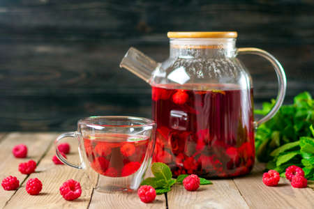Herbal tea with berries, raspberries, mint leaves and hibiscus flowers in glass teapot and cup on wooden table Medicine for cold Vitamin drink Rustic style.の写真素材