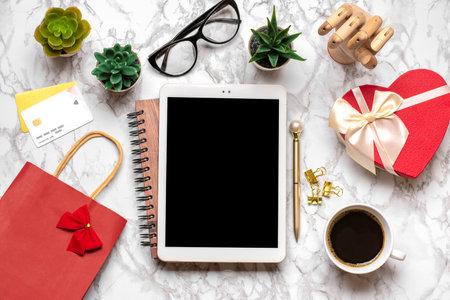 tablet for chooses gifts, makes purchase, cup of coffee, debit card, box, bag, two hearts on marble table Top view Flat lay Holiday shopping list, Happy Valentine's day, online shop concept Mock up.の写真素材