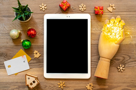 Tablet with black screen, cup coffee, debit card, Xmas decor, snowflakes on wooden table Top view...