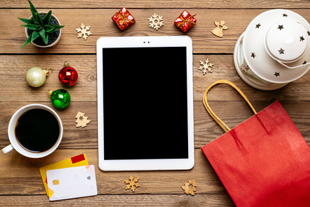 Tablet with black screen, cup coffee, debit card, Xmas decor, snowflakes on wooden table Top view Flat lay Holiday shopping list, Happy New Year, online shop, chooses gifts, makes purchases conceptの写真素材
