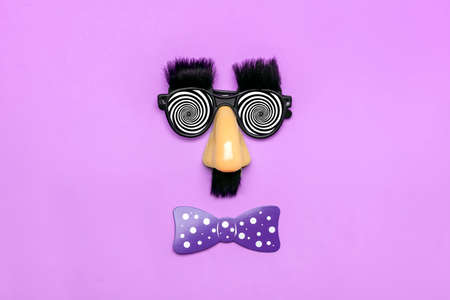 funny face - fake eyeglasses, nose and mustache, confetti, sequins on purple background Happy fools...