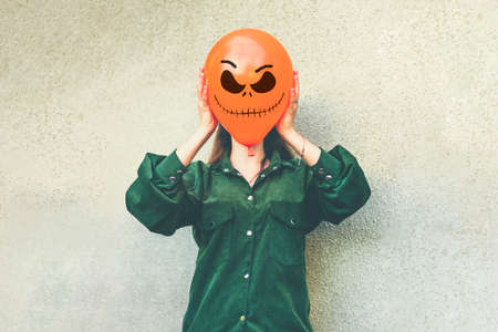 girl in yard holding inflatable balloon with an evil face in her hands outside Happy halloween concept Holiday card Street style Autumn season Costume Jack-o-lantern for carnival.の写真素材