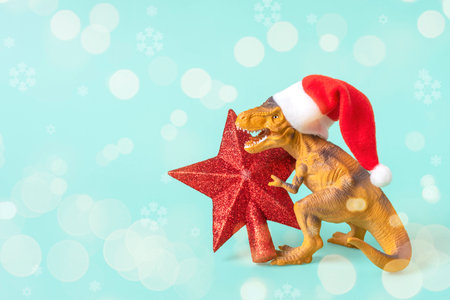 Dinosaur Rex in red Santa Claus hat holds star in its paws on blue background New Years Eve or Christmas Eve Art holiday card Creative idea for Merry xmas concept.の写真素材