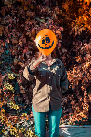 girl in yard holding inflatable balloon with an evil face in her hands outside Happy halloween concept Holiday card Street style Autumn season Costume Jack-o-lantern for carnival.の写真素材