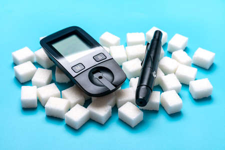 glucometer, sugar cubes on blue background High blood sugar and diabetes concept Top view Flat lay...