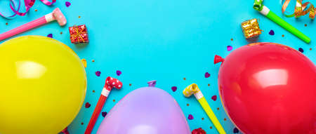 Colorful party frame with red gift box with various party confetti, balloons, streamers, pokers and decorations on blue background. Holiday card Flat lay Top view Happy Birthday party conceptの写真素材