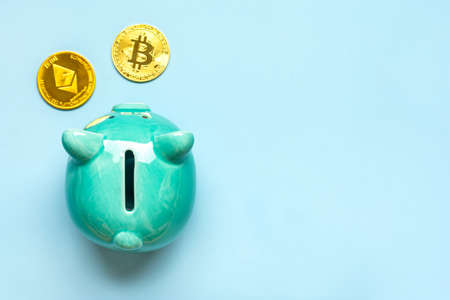 Piggy bank and coins of golden Bitcoin, Ethereum isolated on blue background Accumulation of cryptocurrency, investment in crypto market, business concept Top view Flat lay.の写真素材