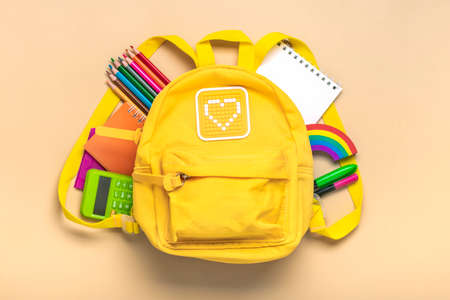 Back to school, education concept Yellow backpack with school supplies - notebook, pens, eraser rainbow, numbers isolated on beige background Top view Copy space Flat lay composition.の写真素材