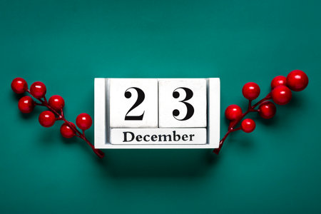 Christmas Eve Date On white wooden cube Calendar, December 23, with Christmas decorations and red berries on green background Xmas holiday card Christmas date.の写真素材
