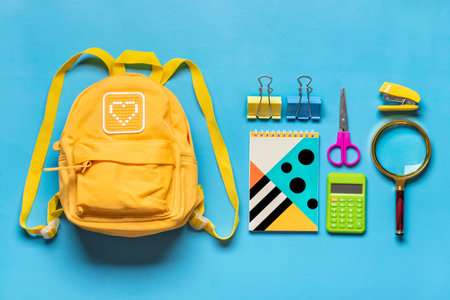 Back to school, education concept Yellow backpack with school supplies - notebook, pens, eraser rainbow, numbers isolated on blue background Top view Copy space Flat lay composition Banner.の写真素材