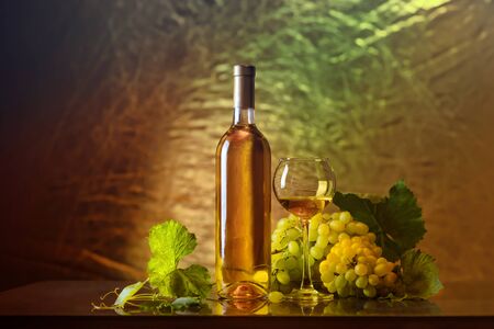 Wine. Bottle and a glass of white wine with ripe grapes still life. White wine on a dark background. The boundaries of art designの写真素材