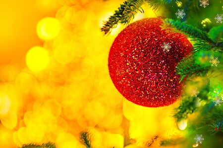 Large red shiny Christmas ball on the fir branch. Beautiful Christmas and New Year Xmas tree border art design. Abstract gold background with Christmas lightsの写真素材