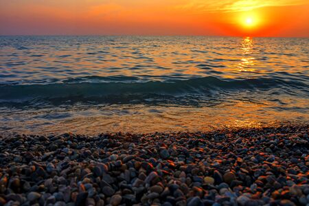Sea sunset. The rocks on the beach and the sea are illuminated by the warm rich sunset sunlightの写真素材